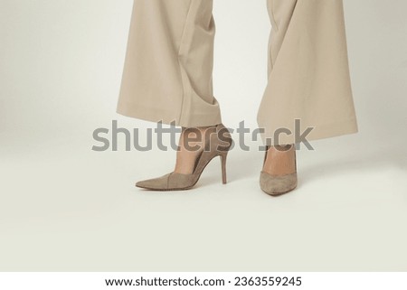 Female model wearing beige smart casual high rise wide leg trousers with high heels. Studio shot.	