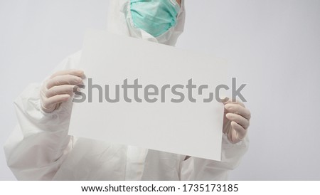 Female model wearing PPE suite and face mask and two hand with gloves is holding A4 paper on white background.