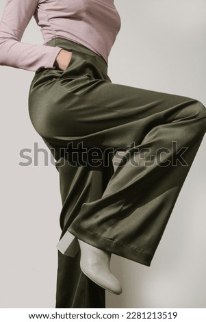 Female model wearing tight viscose long sleeved top and wide green satin trousers. Classic, simple, comfortable yet stylish fashion. Studio shot.	