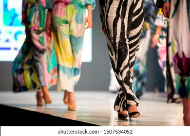 Female Models Walk The Runway In Beautiful Colorful Summer Dresses During A Fashion Show. Fashion Catwalk Event Showing New Collection Of Clothes. Unrecognizable People. Legs And Shoes Only.