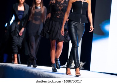 Female models walk the runway in beautiful designer dresses during a Fashion Show. Fashion catwalk event showing new collection of clothes. High heels shoes. Legs only. Black Leather Leggings Bottoms.