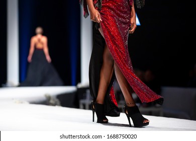 Female Models Walk The Runway In Beautiful Red Dress During A Fashion Show. Fashion Catwalk Event Showing New Collection Of Clothes. Unrecognizable People. High Heels Shoes. Legs Only. Red Dress.