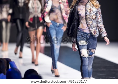 Female models walk the runway in different dresses during a Fashion Show. Fashion catwalk event showing new collection of clothes. In a row.