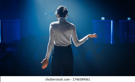 Female Motivational Speaker On Stage, Talking About Happiness, Diversity, Success, Leadership, STEM And How To Be Productive. Woman Presenter Leads Tech Business Conference. Back View Shot