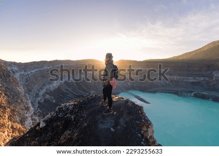 female mountaineer contemplating the Poas Volcano Crater Lagoon at sunrise surrounded by volcanic rocks in Poas Volcano National Park in Alajuela province of Costa Rica