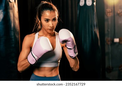 Female muay thai boxer in defensive guard stance wearing glove in the gym ready to fight posing, boxing training and professional martial art sport. Impetus - Powered by Shutterstock