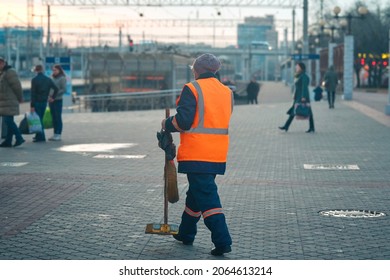 Female Municipal Worker Cleaning Railway Station. Cleaner Sweeping Pedestrian Zone At Train Station In Evening. Utility Worker Sweep Sidewalk