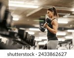 A female muscular bodybuilder is exercising with dumbbell in a gym.