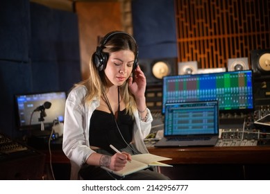 Female music producer listening to music and taking notes in notepad. Young Caucasian woman working in sound recording studio. Creating music concept - Powered by Shutterstock