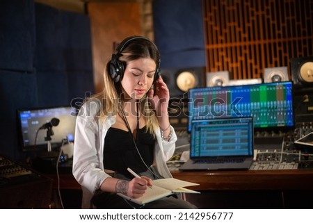 Female music producer listening to music and taking notes in notepad. Young Caucasian woman working in sound recording studio. Creating music concept