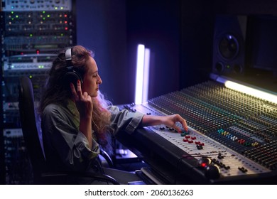 Female musical producer in headphones writing music on music keyboard in the studio