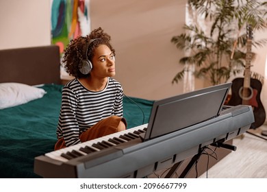 Female musician in headphones sitting on bed in front of electronic musical instrument while spending time at home - Powered by Shutterstock