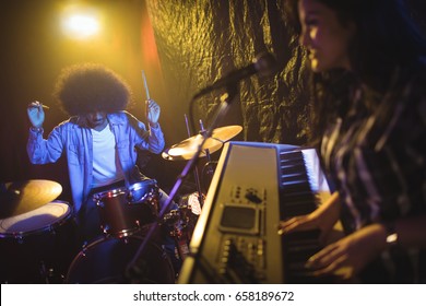 Female musician playing piano with male drummer in illuminated night club - Powered by Shutterstock