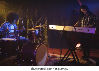 Female musician playing piano with male drummer in night club - Powered by Shutterstock