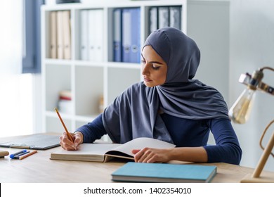 Female Muslim professor taking a note in a book, getting ready for classes. Woman fully absorbed in work.