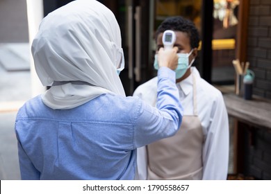 Female Muslim Retail Business Staff Or Grocery Shop Keeper Checking Fever Of Black African Customer By Portable Thermo Scan Device