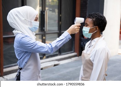 Female Muslim Retail Business Staff Or Grocery Shop Keeper Checking Fever Of Black African Customer By Portable Thermo Scan Device