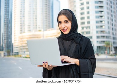 Female Muslim Student In Abaya Holding Laptop Outdoors