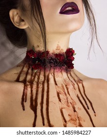 female neck with red bloody roses and blood drops which drips on pale skin. close-up portrait of young girl with dark halloween make up. halloween concept. free space