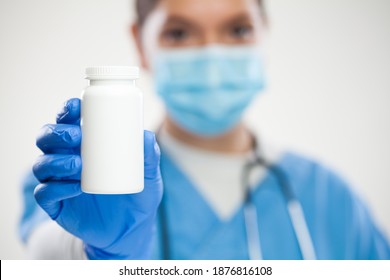 Female NHS GP UK General Practitioner Doctor,wearing Scrubs,protective Face Mask And Gloves,holding White Blank Bottle Of Pills,empty No Label Container Suitable For Adding Custom Text,selective Focus