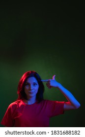 Female Night Portrait. Mind Blown. Stress Anxiety. Mental Disorder. Insane Woman Pointing Finger At Temple In Red Blue Neon Light Isolated On Dark Green Empty Space Background.