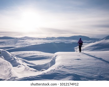 Female in the norwegian mountains at easter resting at the edge of a snowdrift during a ski adventure looking at the sun covered by light clouds 