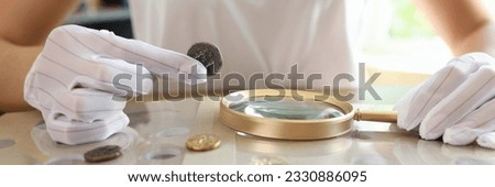 Female numismatist examines collection of coins. Woman looks at coins through magnifying glass. Numismatic collection review.