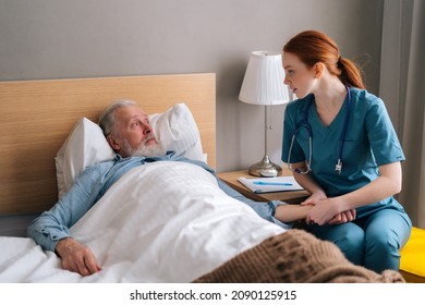 Female Nurse Checking Pulse On Wrist To Sick Senior Male Patient Lying On Bed In Hospital Room. Doctor Checking Mature Patient Pulse At Home. Elderly Man Getting Medical Consultation In Hospice.