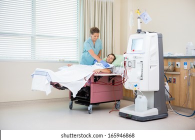 Female Nurse Covering Male Patient Receiving Renal Dialysis With Blanket In Hospital Room