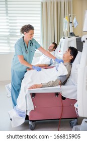 Female Nurse Covering Patient Undergoing Renal Dialysis With Blanket In Hospital Room