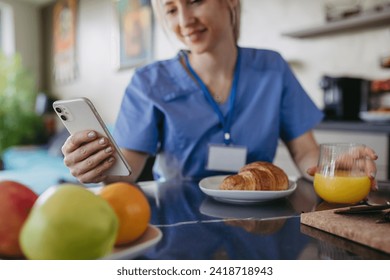 Female nurse or doctor getting ready for work in the morning, scrolling on smartphone while eating breakfast. Work-life balance for healthcare worker. - Powered by Shutterstock