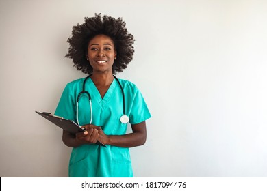 Female nurse or doctor smiles while staring out window in hospital hallway and holding clipboard with patient file. African American female pediatric nurse in office. Portrait Of Female Nurse Standing