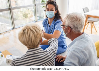 Female Nurse Greeting With Seniors Patients With Mask While Being In A Home Visit.