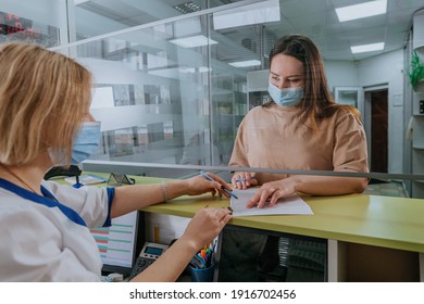 Female nurse help patient to fill form at hospital reception. Nurse and patient wearing protective face masks and using protective glass screen. New normal during Pandemic COVID-19 concept. - Powered by Shutterstock