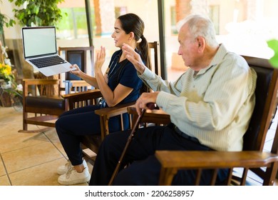 Female Nurse Helping An Elderly Man In His 80s At The Nursing Home To Chat With His Family During An Online Video Call