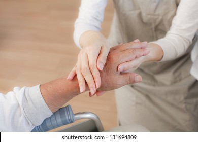 Female Nurse Massaging Arthritic Hands Of Elderly Man At Retirement Community Center.