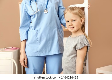 Female Nurse Measuring Height Of Little Girl In Hospital