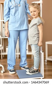 Female Nurse Measuring Height Of Little Girl In Hospital