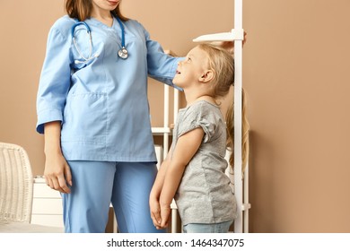 Female Nurse Measuring Height Of Little Girl In Hospital