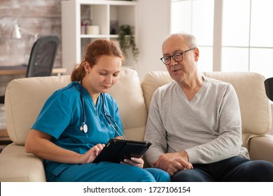 Female Nurse In Nursing Home Helping Old Man To Use Tablet Computer.