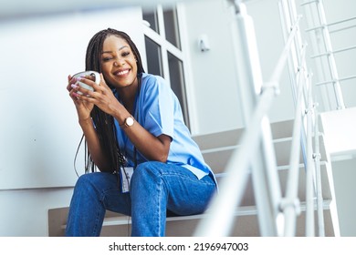 Female Nurse On Coffee Break In Hospital. Overworked Nurse In Scrubs With Face Mask Takes Coffee Break In Busy Hospital During Health Pandemic.  Female Nurse Takes A Break Outside Of A Hospital