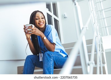 Female Nurse On Coffee Break In Hospital. Overworked Nurse In Scrubs With Face Mask Takes Coffee Break In Busy Hospital During Health Pandemic.  Female Nurse Takes A Break Outside Of A Hospital