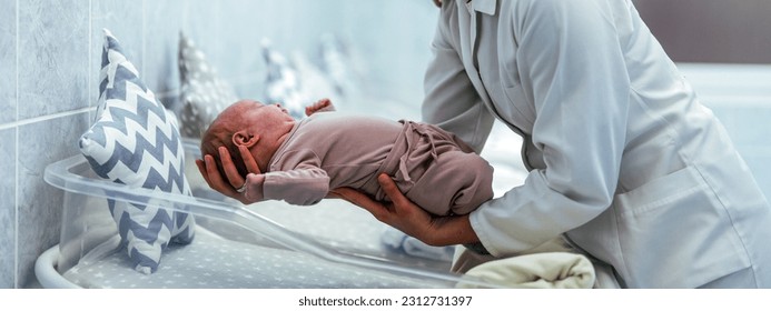 Female nurse with premature born baby in intensive care unit holding infant in her hands. Pediatrician nurse taking care of newborn baby at hospital ward. She is holding baby while mother is resting. - Shutterstock ID 2312731397