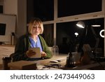 Female nurse with tablet computer working evening shift at table in clinic