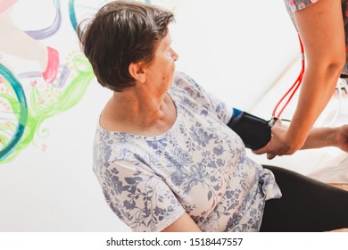 Female Nurse Taking Blood Pressure From Senior Woman In The Hospital - Doctor With Stethoscope Checking Vital Signs Of Cute Old Lady In A Private Clinic