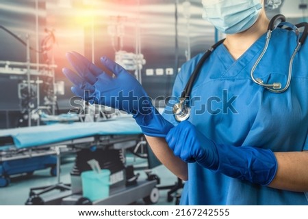Female nurse wear blue uniform with a mask putting on rubber latex blue gloves  to complicated surgical operation