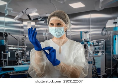 A female nurse wears a blue uniform with a mask while putting on rubber latex blue gloves during a complex surgical operation. medicine. doctors operating room - Powered by Shutterstock