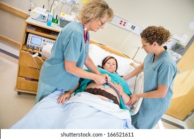 Female Nurses Preparing Pregnant Woman For Fetal Heart Rate Monitor In Hospital Room