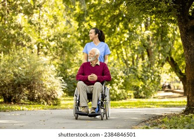 Female nursing assistant and elderly man in wheelchair enjoying autumn in the park. - Powered by Shutterstock