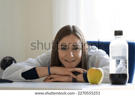 Female nutritionist smiles at camera and shows an apple and a water bottle. Healthy eating concept